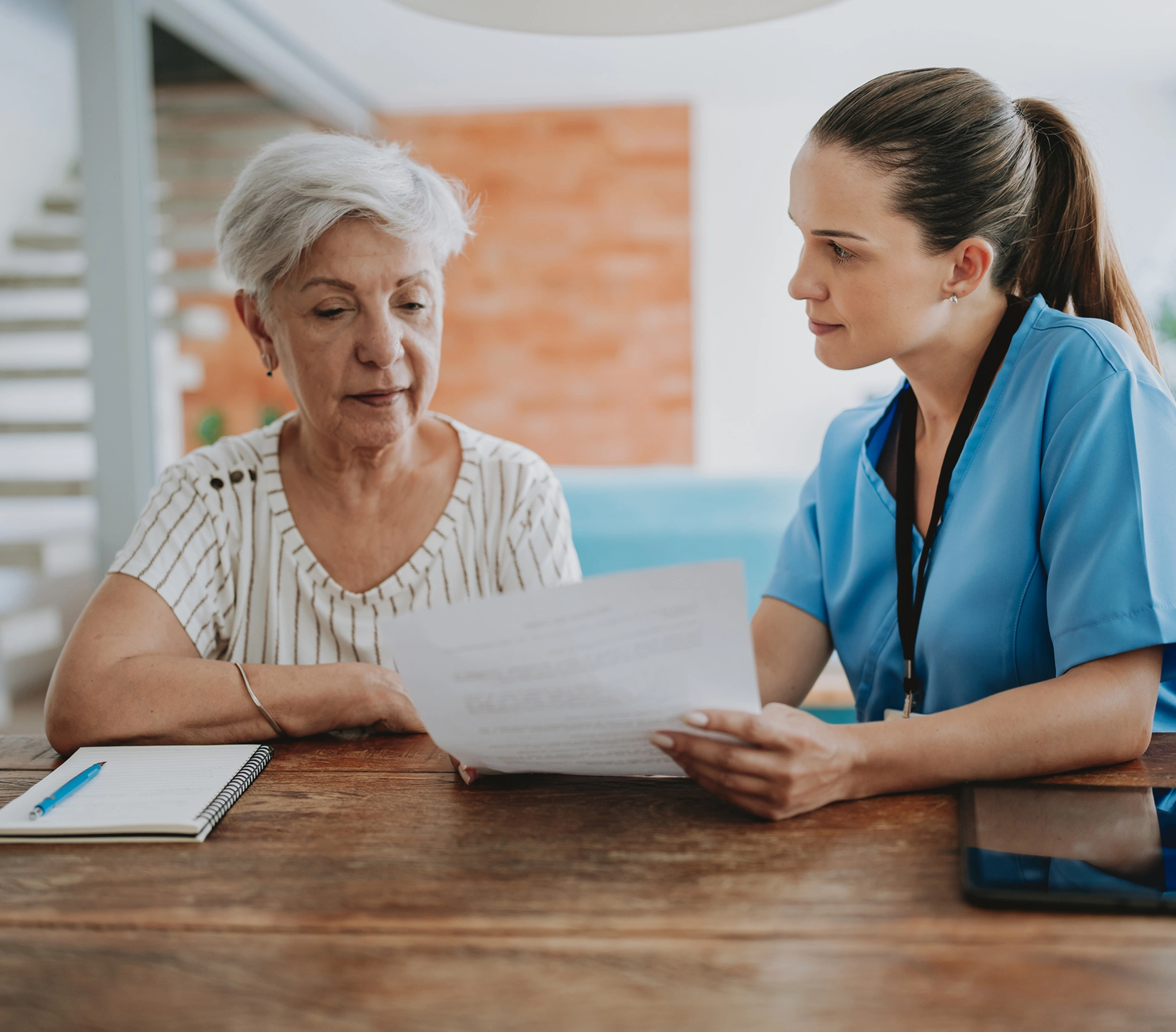 Female doctor wearing a stethoscope and holding a clipboard, talking to an older woman
