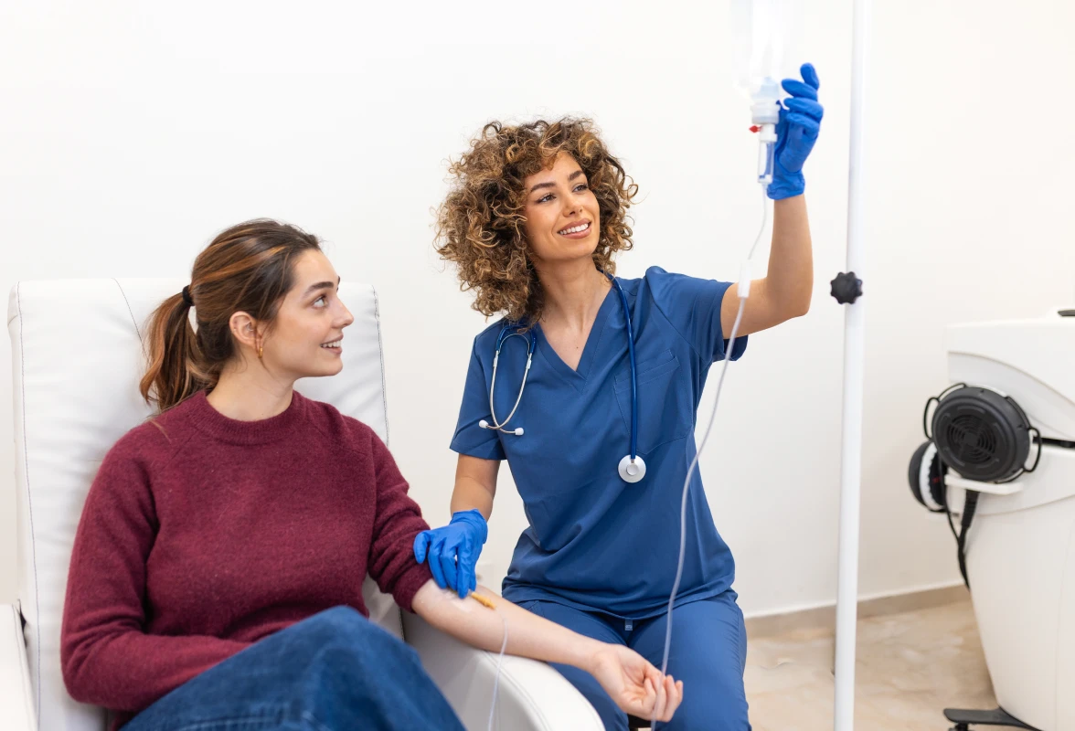Woman sitting in a chair with a nurse standing beside her, holding an IV drip
