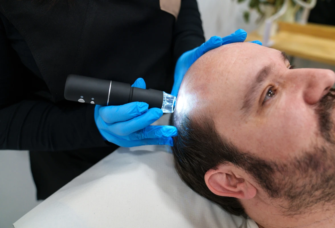 Man lying on a white surface while a person wearing blue gloves holds a black object in their hand