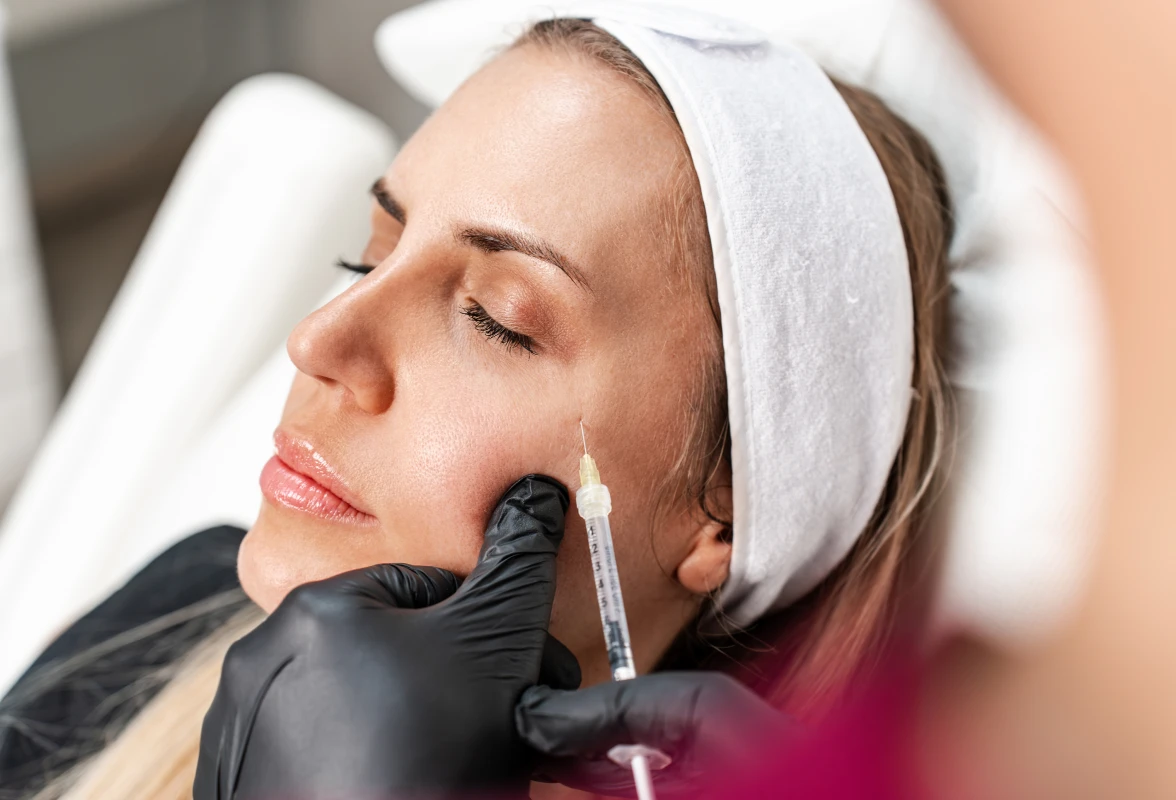Woman getting a botoxeti injection on her face, with a white cloth draped over her head and a blurred background
